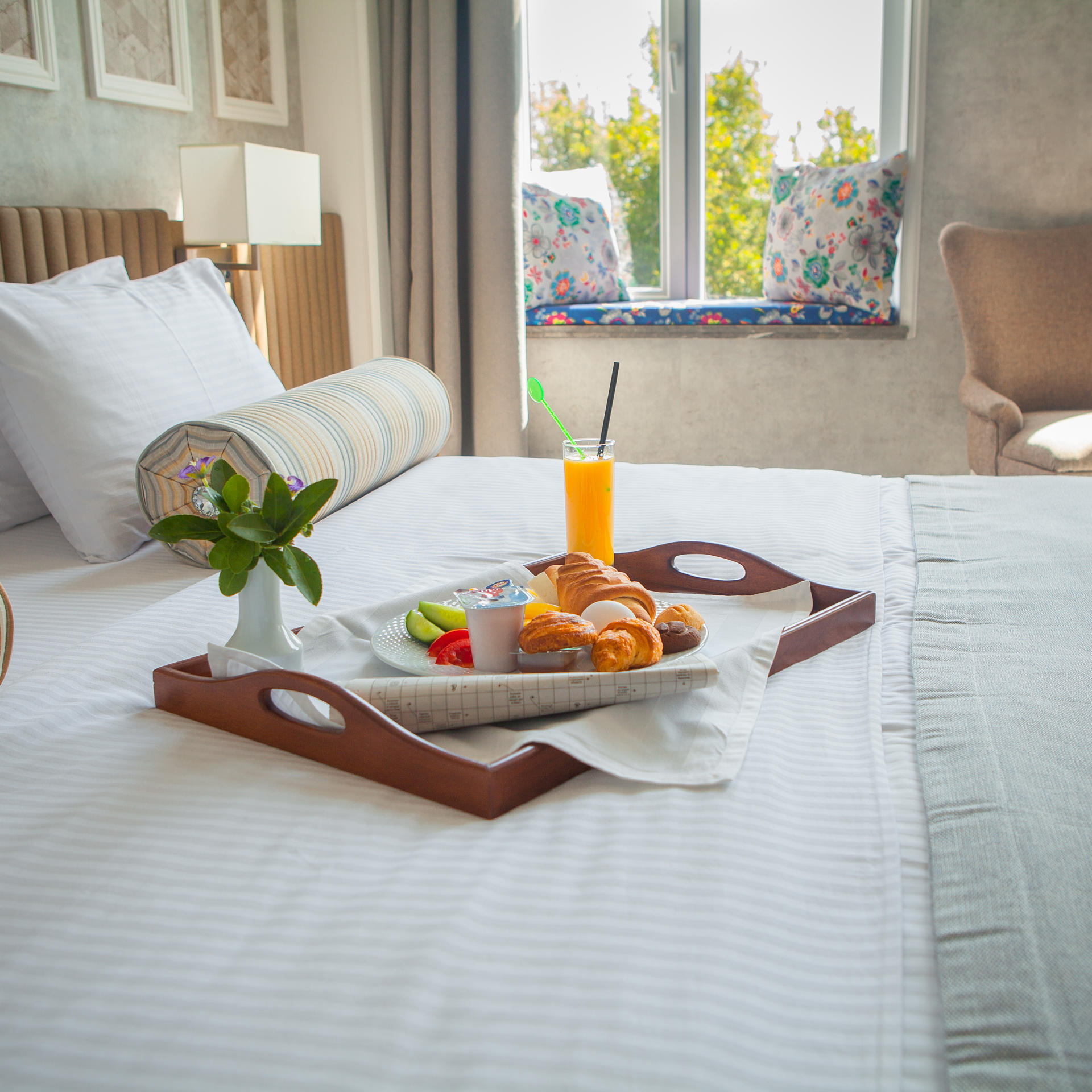 Croissant, boiled egg, orange juice, yogurt breakfast on tray in bed in hotel room 1